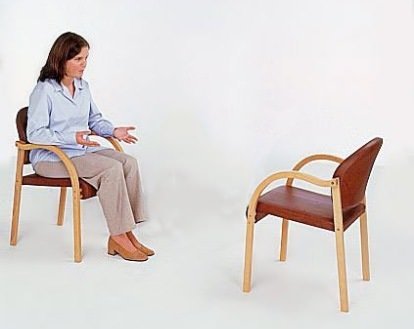 Two empty wooden chairs facing each other in a calm, modern, sunlit room.
