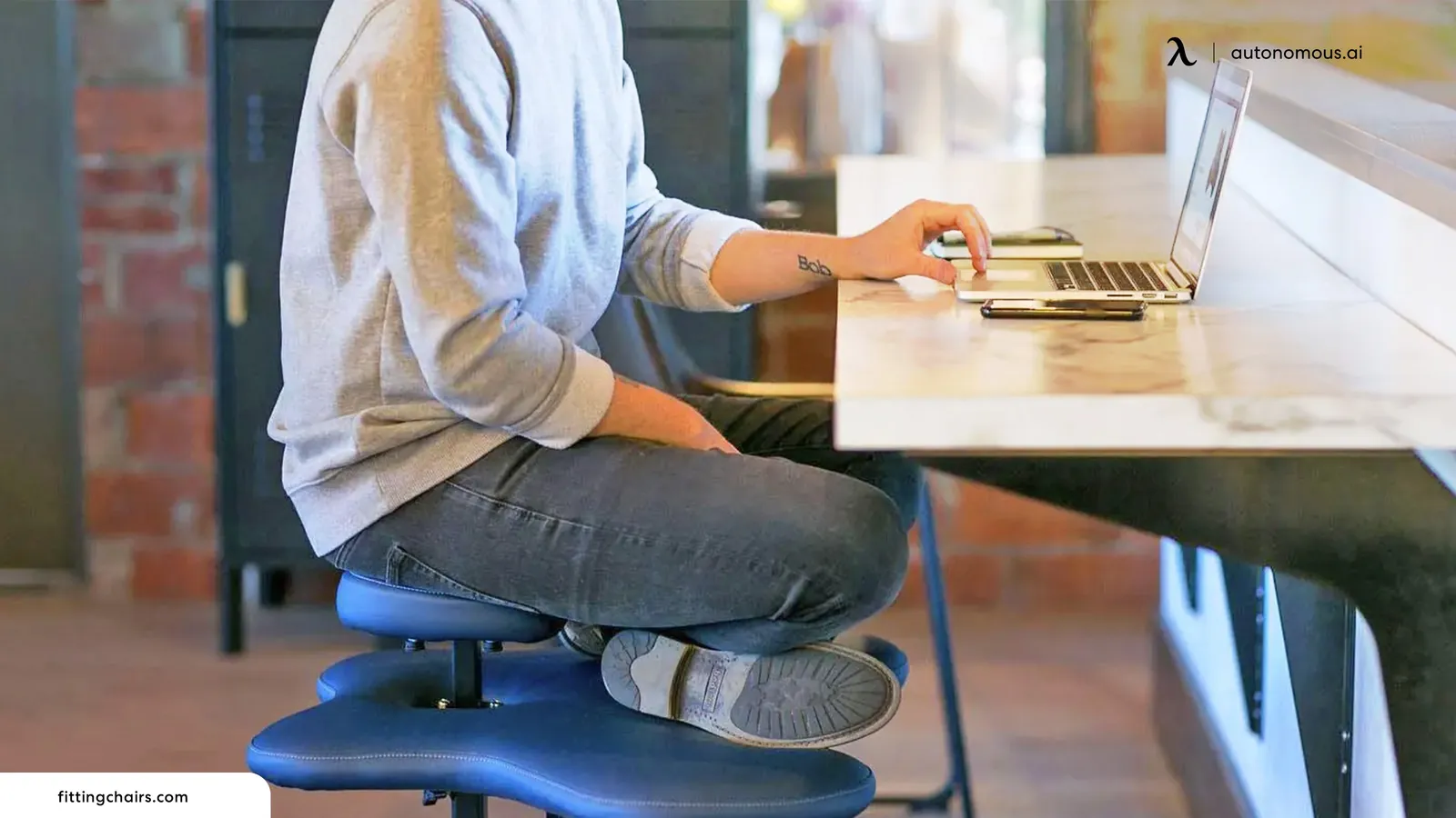 An active saddle stool with a split seat beside a standing desk.