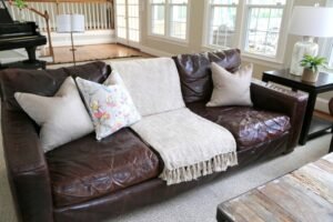 A bright and modern living room featuring a well-styled brown sofa with light accessories.