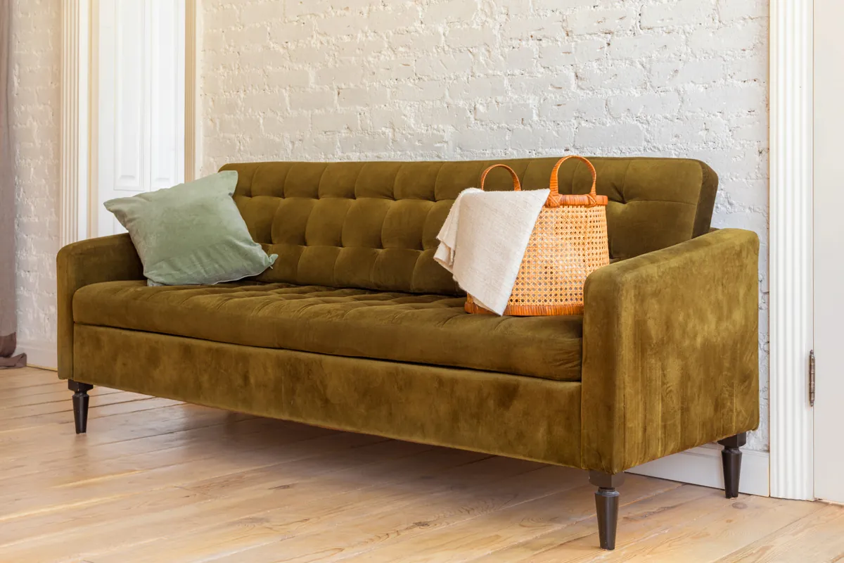 A deep-seated velvet couch stuck in a narrow residential hallway.