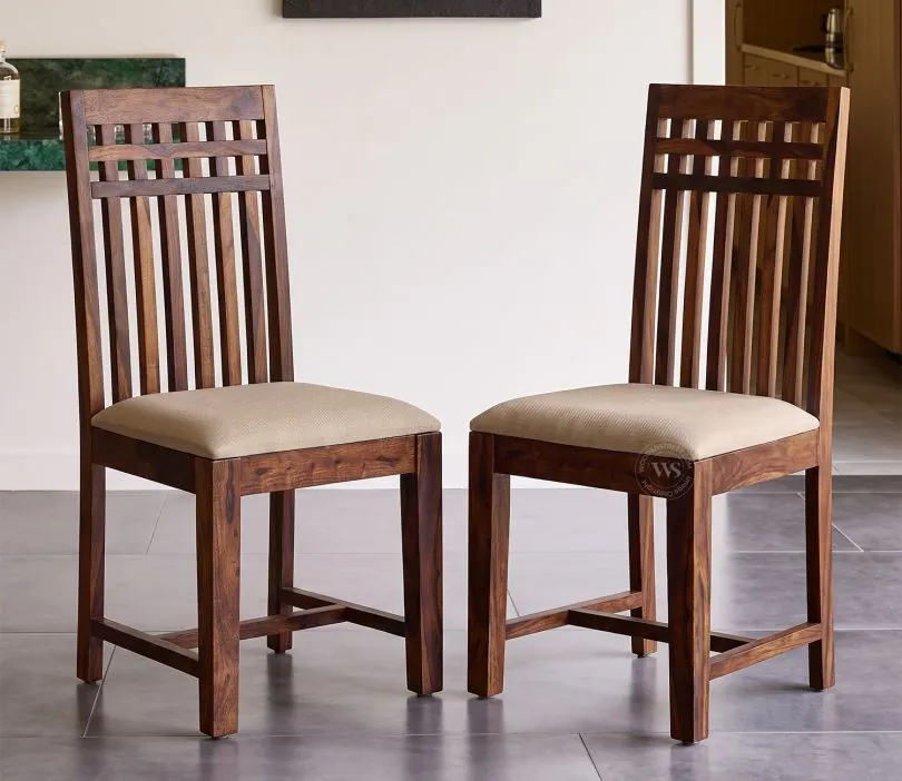 Four matching inexpensive wooden dining chairs lined up in a sunlit apartment.