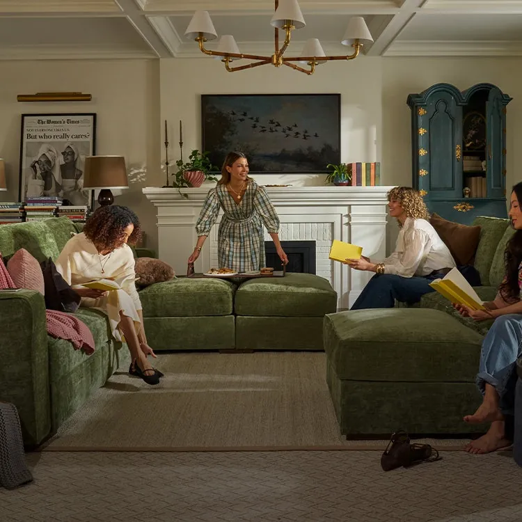 Hands carefully connecting two modular sectional couch pieces together in a sunlit room.
