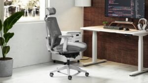 A modern ergonomic swivel chair sits at a desk in a bright office.