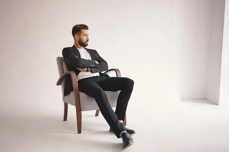 A person practicing a natural pose while sitting on a high studio stool.