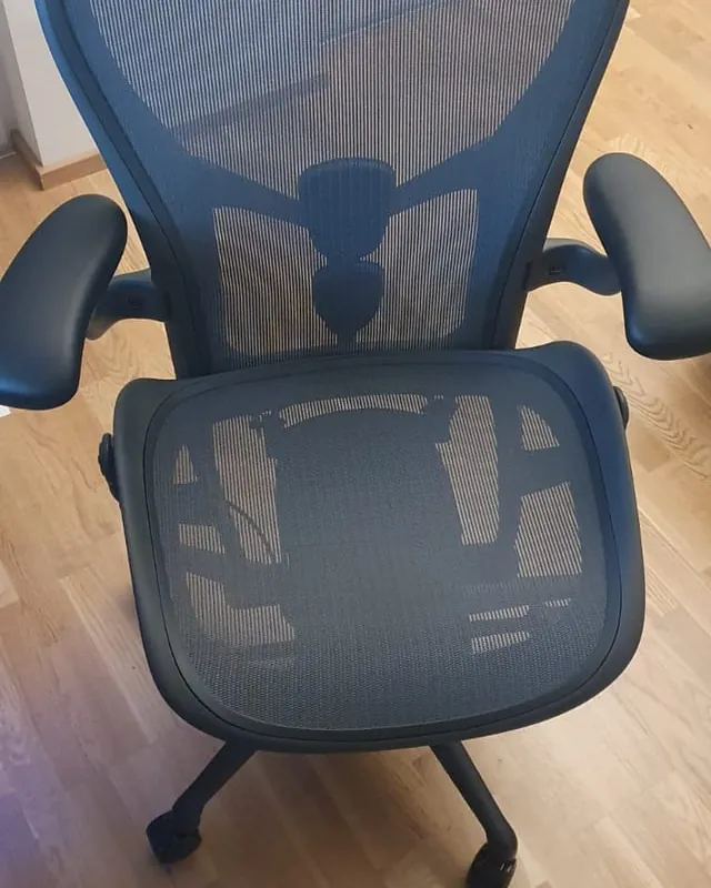 A person sitting improperly on the edge of a C-chair at a desk.